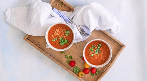 Zwei Schälchen mit Tomatensuppe mit Reis von oben fotografiert auf einem Tablett, daneben Tomaten