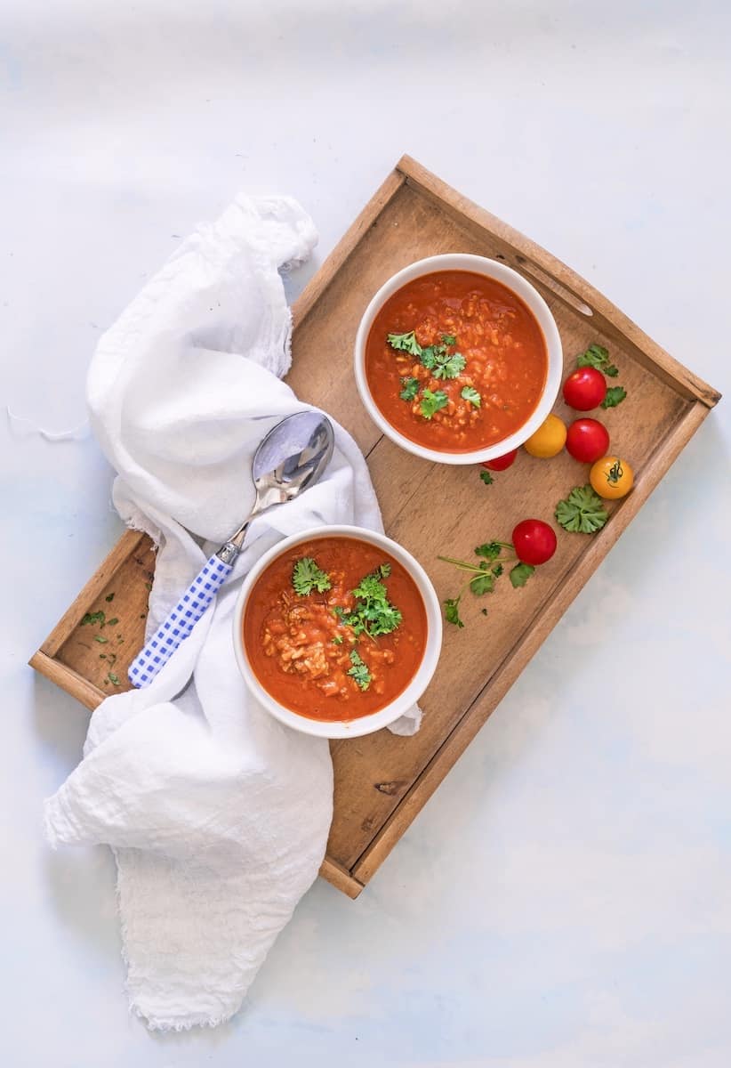 Zwei Schälchen mit Tomatensuppe mit Reis von oben fotografiert auf einem Tablett, daneben Tomaten