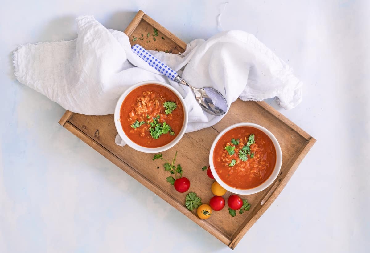 Zwei Schälchen mit Tomatensuppe mit Reis von oben fotografiert auf einem Tablett, daneben Tomaten