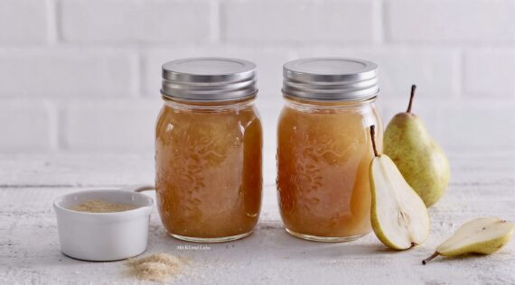 Zwei Gläser mit hell orangefarbender Marmelade, daneben liegen zwei Birnen