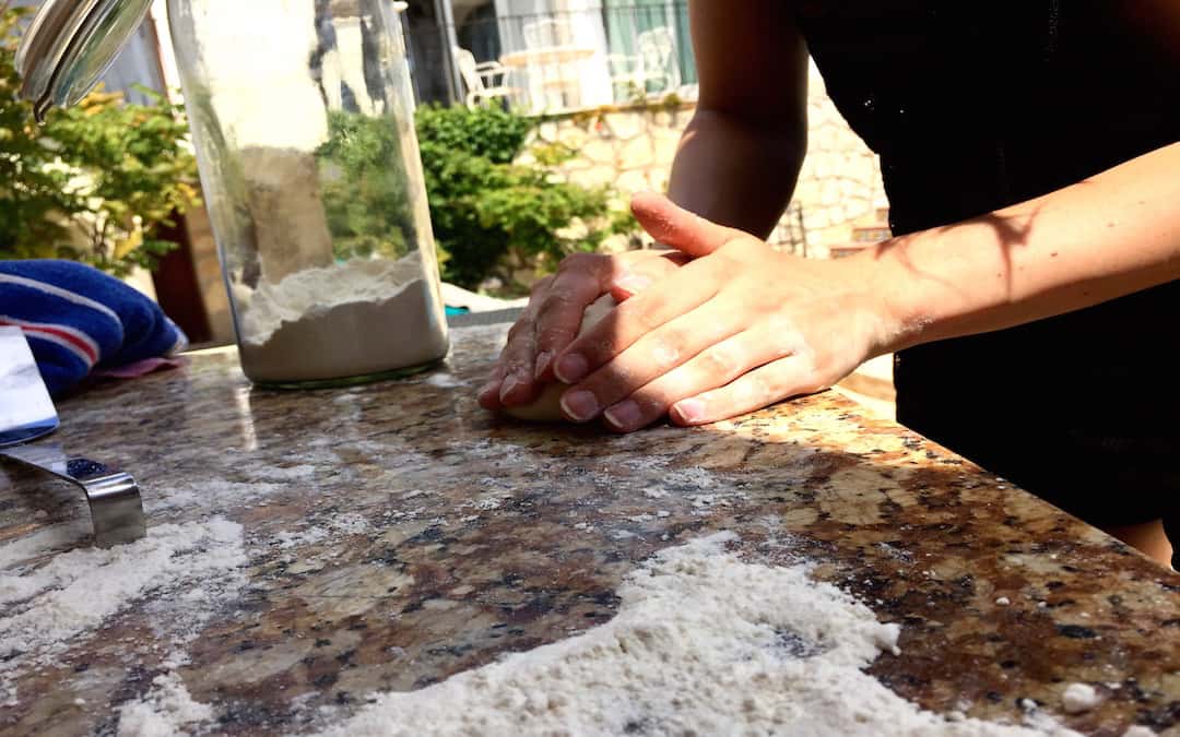 Eine Teigkugel wird von zwei Händen umschlossen und auf einer Steinplatte geknetet. 