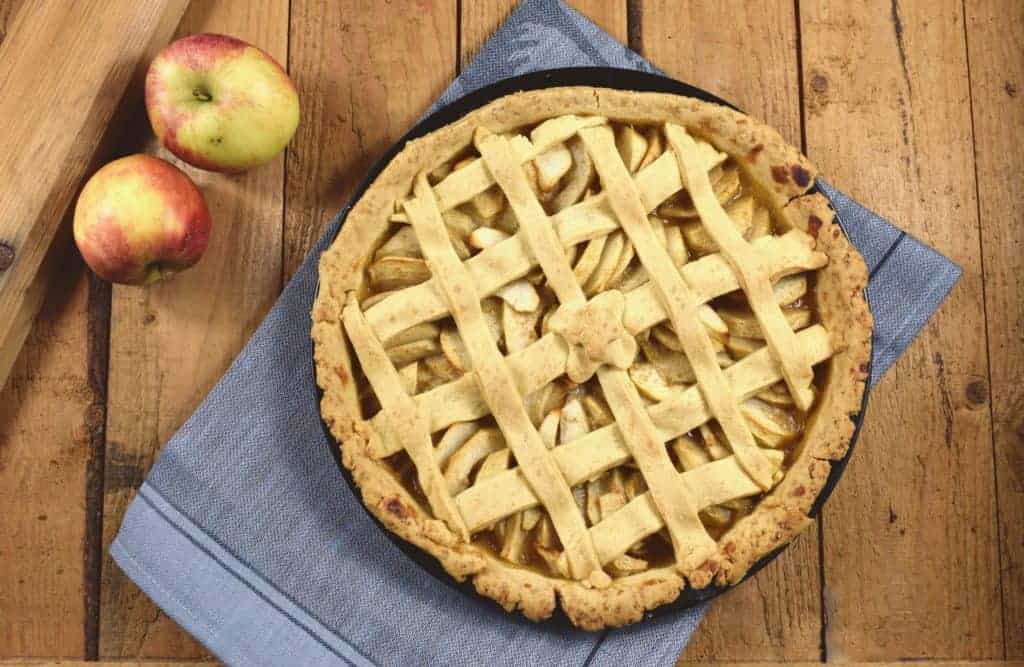 Apple Pie auf Holzuntergrund von oben fotografiert mit zwei Äpfeln daneben
