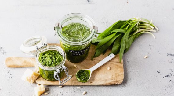 Zwei Gläser Bärlauch-Pesto auf einem Holzbrett, daneben frischer Bärlauch