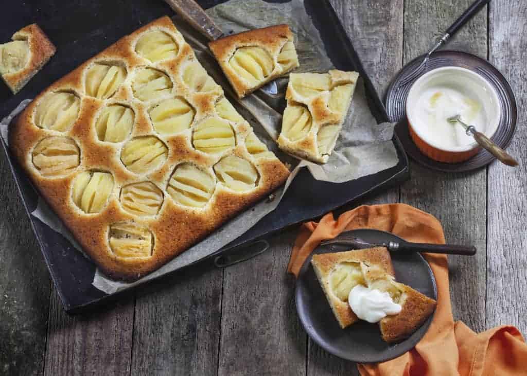 Angeschnittener Apfelkuchen auf schwarzem Blech mit angestellter Creme