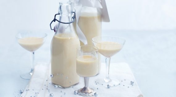 Zwei Flaschen mit hellem Likör, daneben drei Gläser mit dem gleichen Getränk