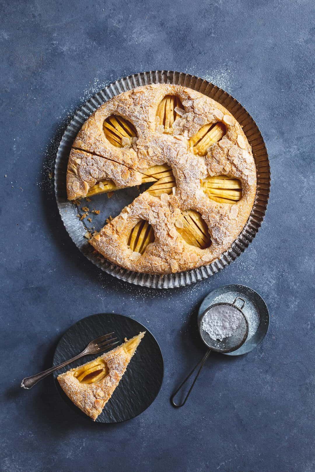 Apfelkuchen mit versunkenen Äpfeln, angeschnitten auf grauem Untergrund
