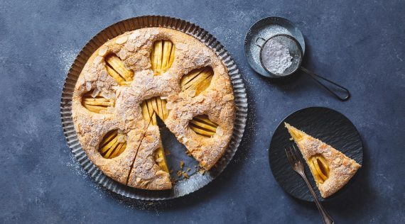 Apfelkuchen mit versunkenen Äpfeln, angeschnitten auf grauem Untergrund