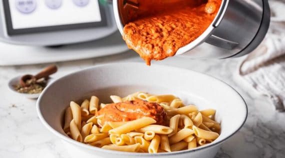 Jemand gießt Tomatensoße aus dem Mixtopf des Thermomix® auf einen Teller mit Nudeln – Foto: Anna Gieseler