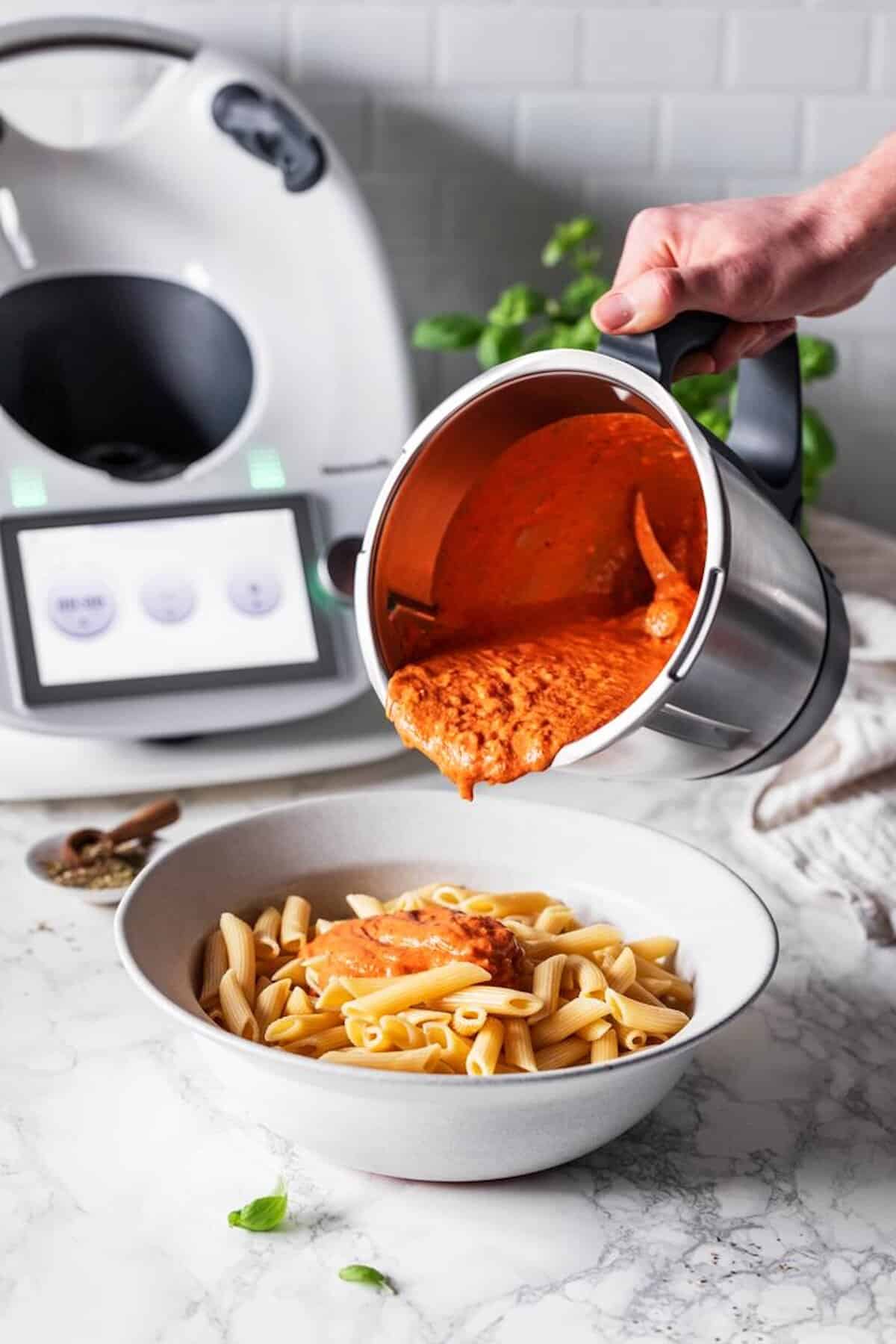 Jemand gießt Tomatensoße aus dem Mixtopf des Thermomix® auf einen Teller mit Nudeln – Foto: Anna Gieseler