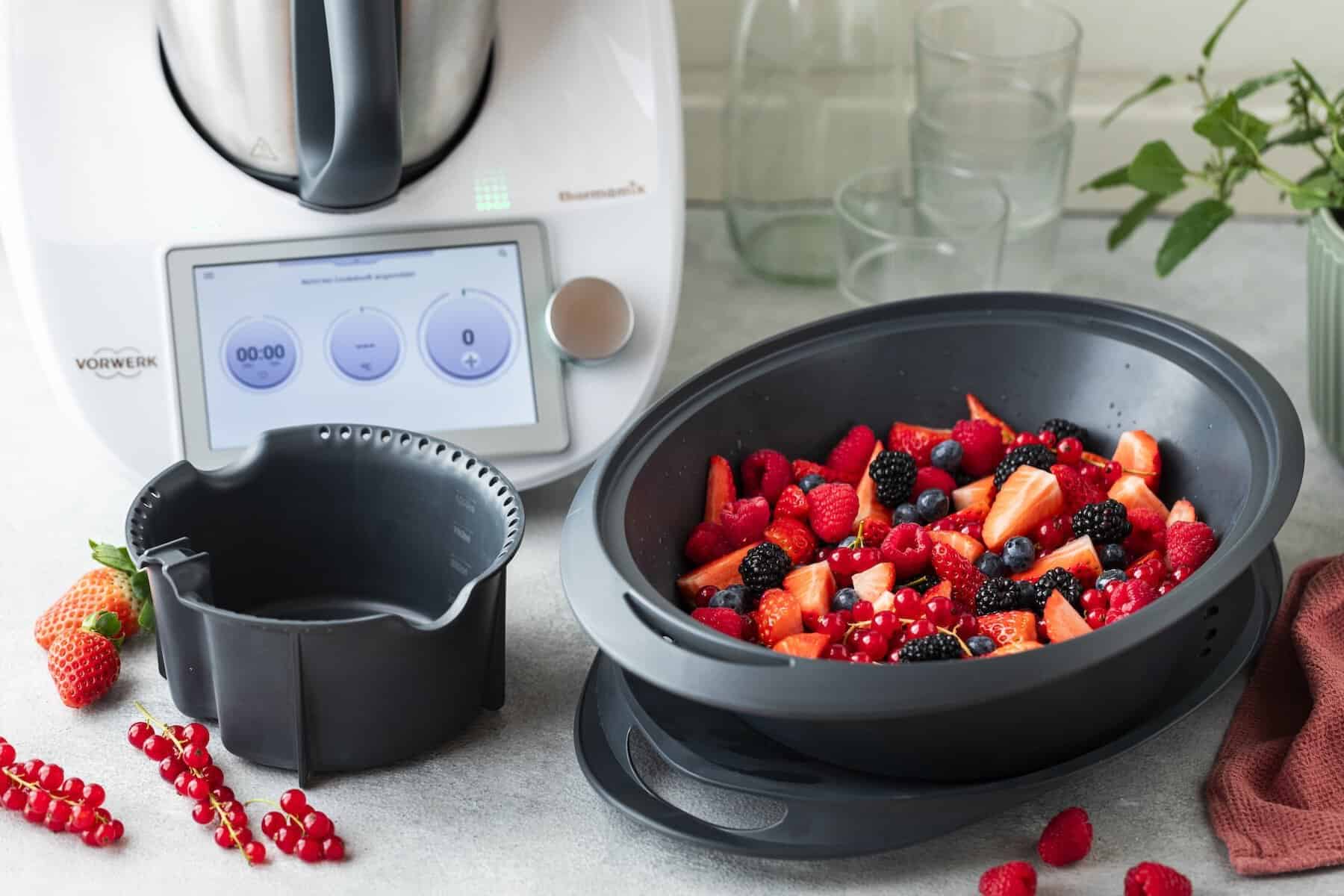 Thermomix® mit Früchten im Varoma®, daneben ein einsatz zum Auffangen des Saftes
