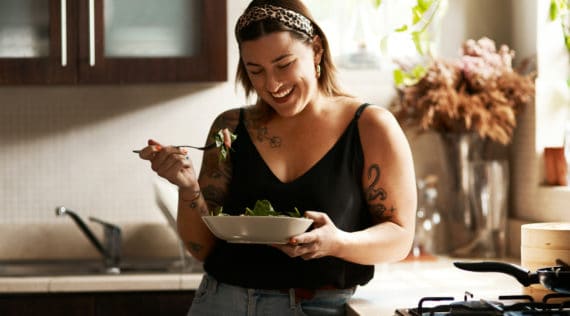 Tättowierte Frau in hemischerKüche mit Salatschüssel in der Hand