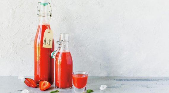 Zwei Flaschen mit rotem Erdbeer-Limes und ein Glas vor grauem Hintergrund – Foto: Désirée Peikert
