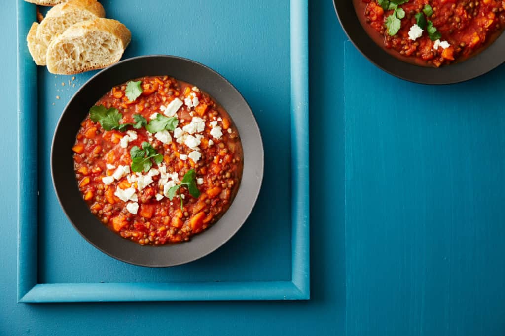 Schwarzer Teller mit Kürbis-Linsen-Chili mit angelegten Baguettescheiben