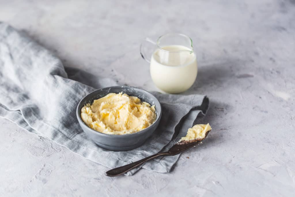 Butter im dunklen Schälchen mit angestellter Sahne in Glasflasche