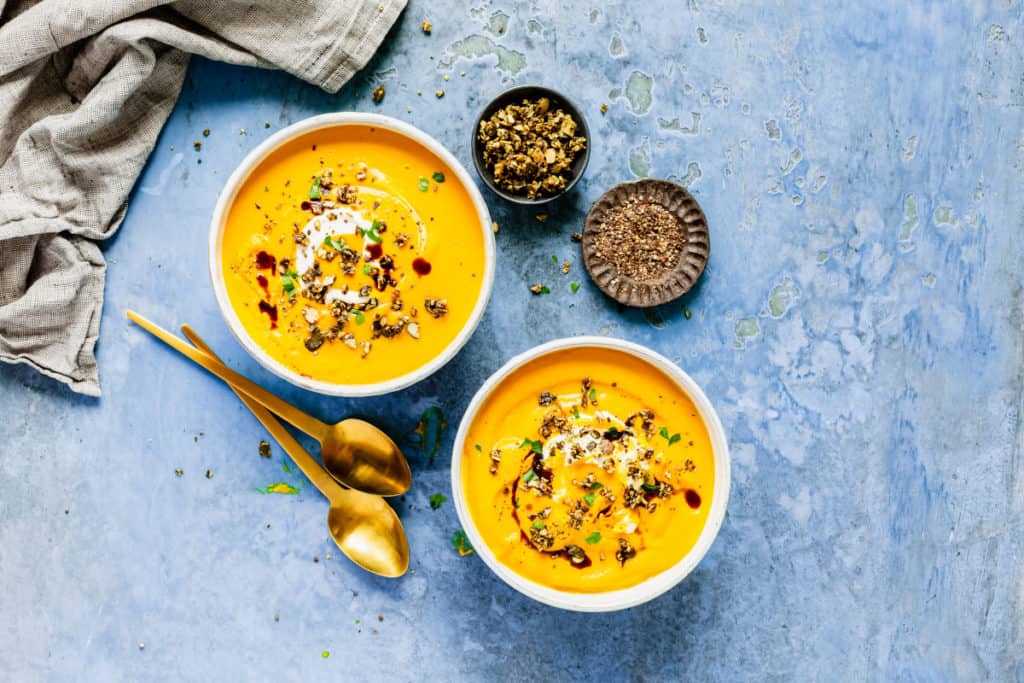 Zwei Schüsseln mit Kürbissuppe auf blauem Untergrund