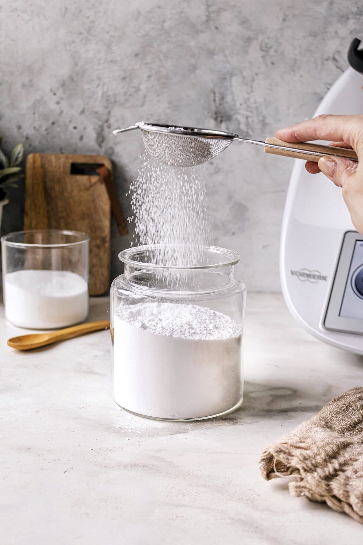 Ein Glas mit Puderzucker, in da noch mehr Zucker hineinrieselt. Daneben steht ein Thermomix® – Foto: Sandra Leibinger