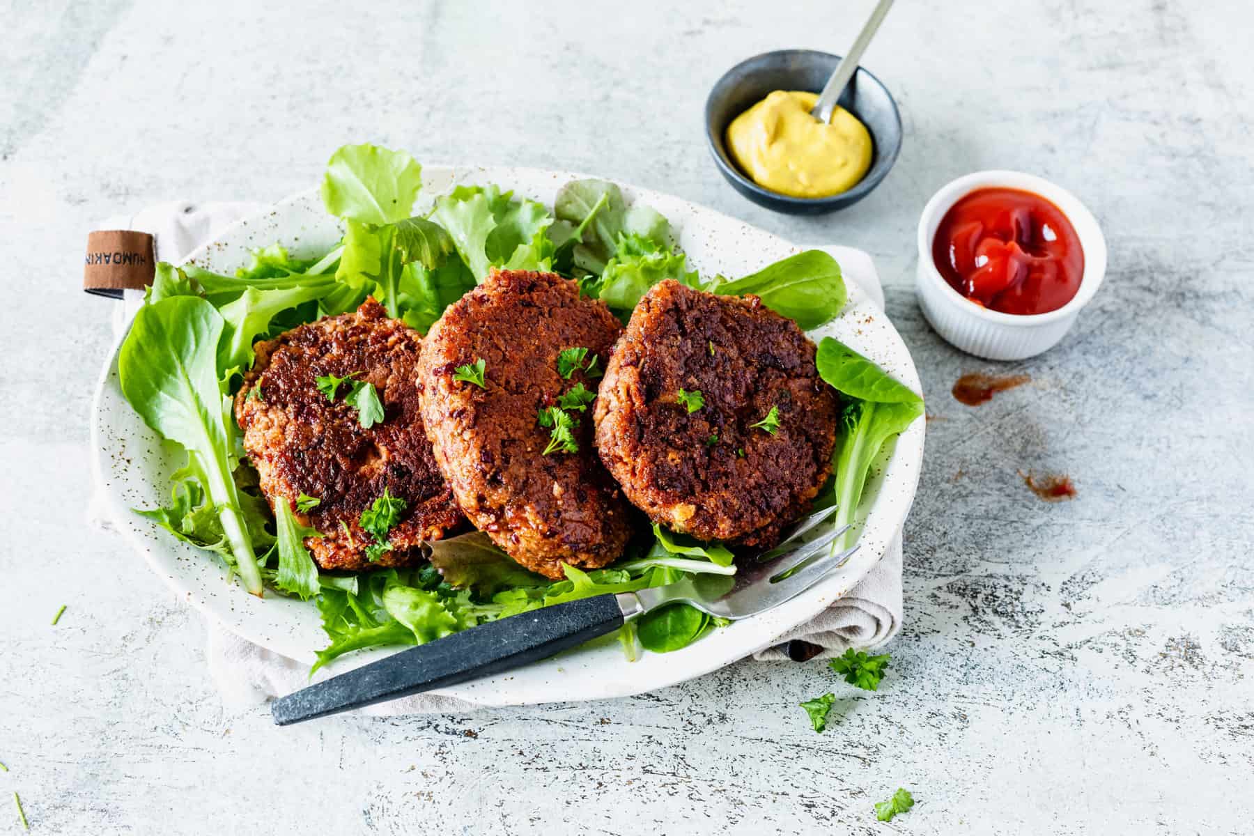 Drei vegetarische Frikadellen auf einem Salatbett mit Senf und Ketchup