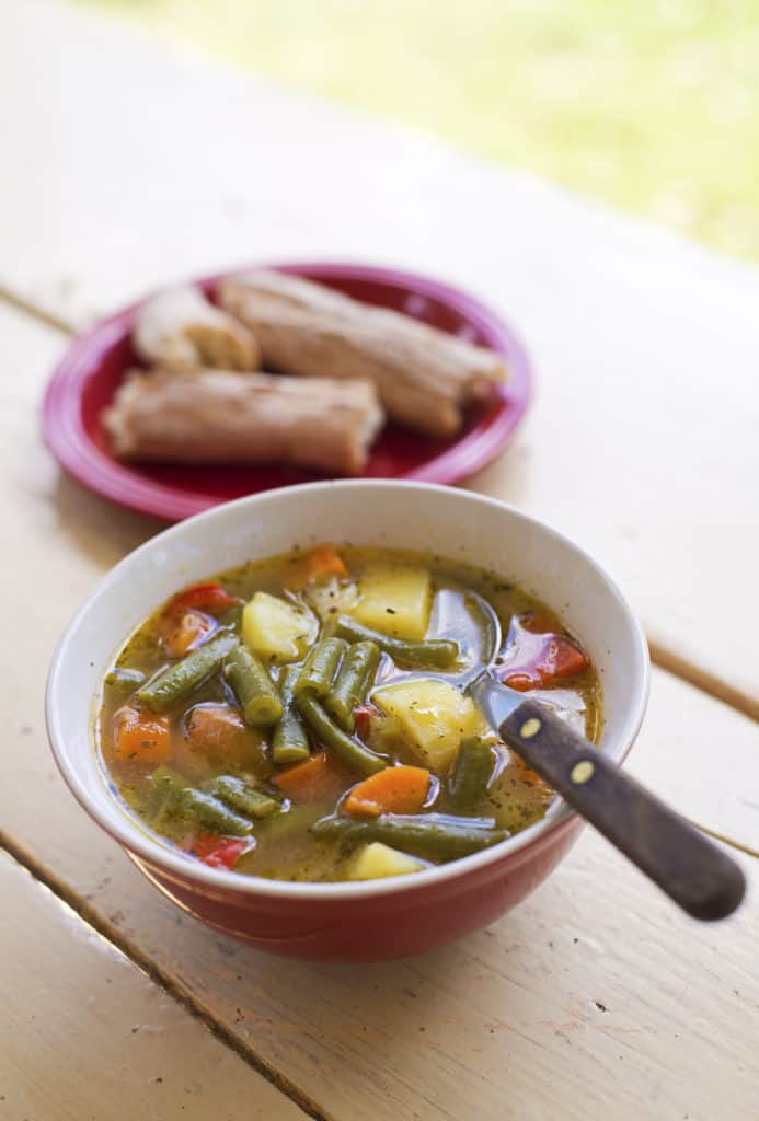 Bohnensuppe mit Kartoffeln und Möhren in einer roten Schüssel, daneben Brot auf einem Teller