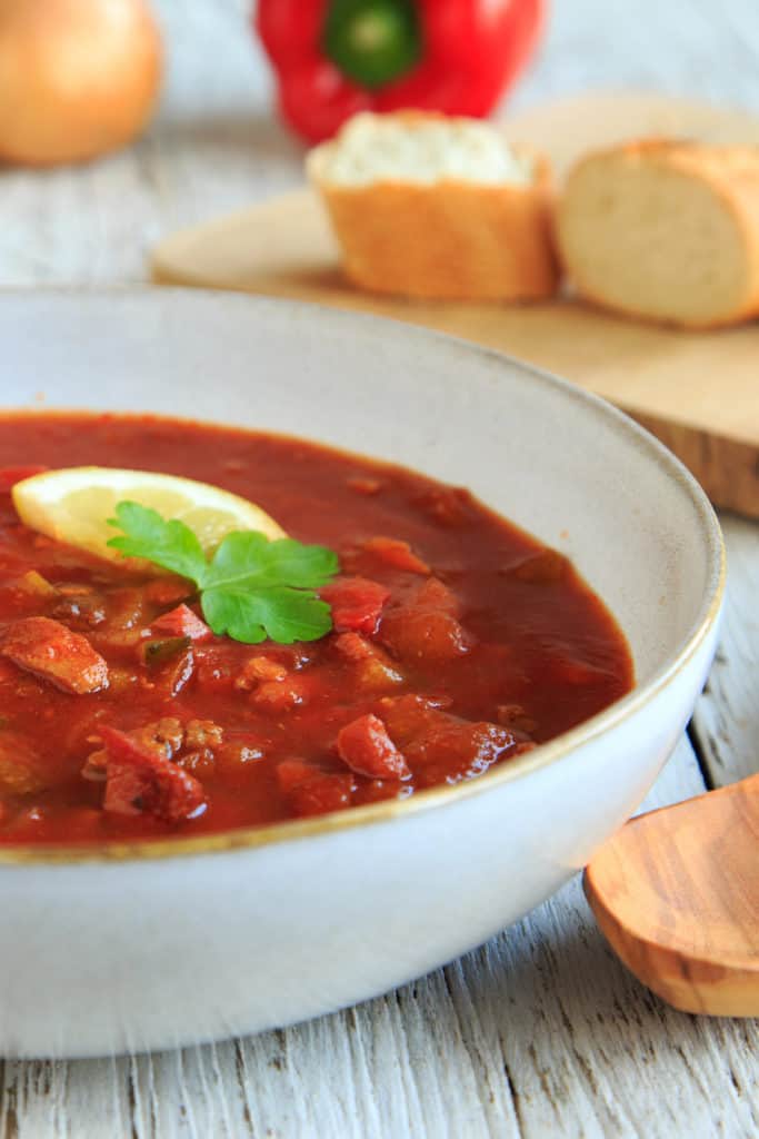 Soljanka-Suppe in einem weißen Teller, garniert mit Zitrone und Petersilie