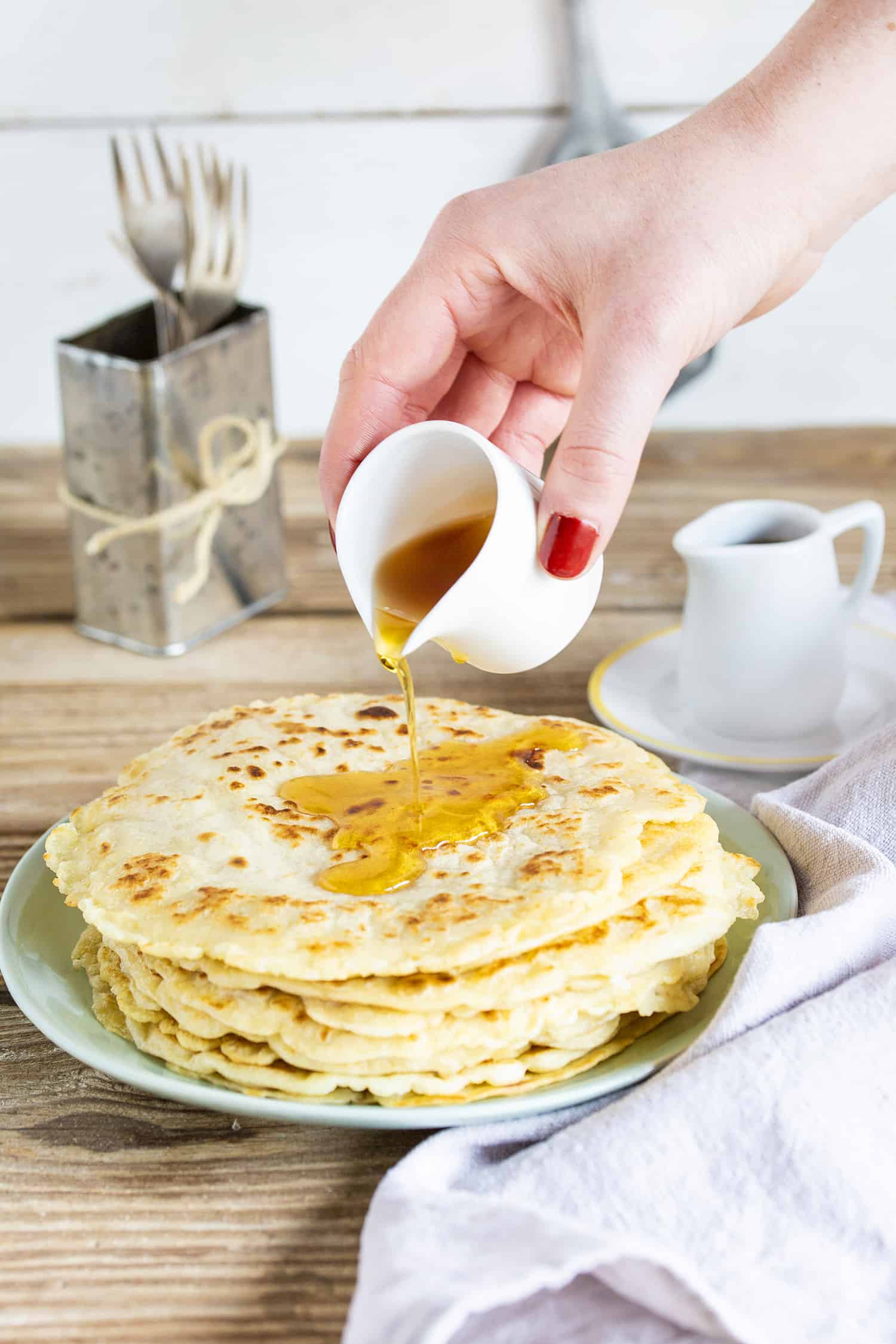 Vegane Pfannkuchen gestapelt, eine Hand hält ein Kännchen mit Sirup, der darüber läuft