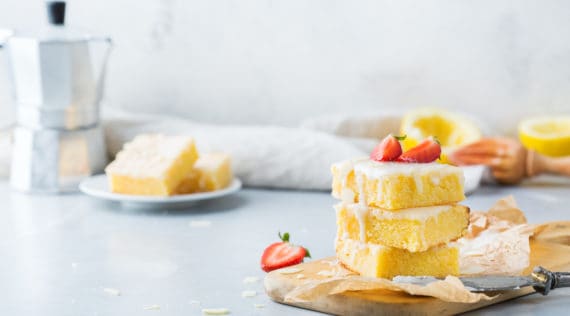 Drei Stück Zitronen-Blechkuchen mit Zuckerguss gestapelt auf einem Holzbrettchen