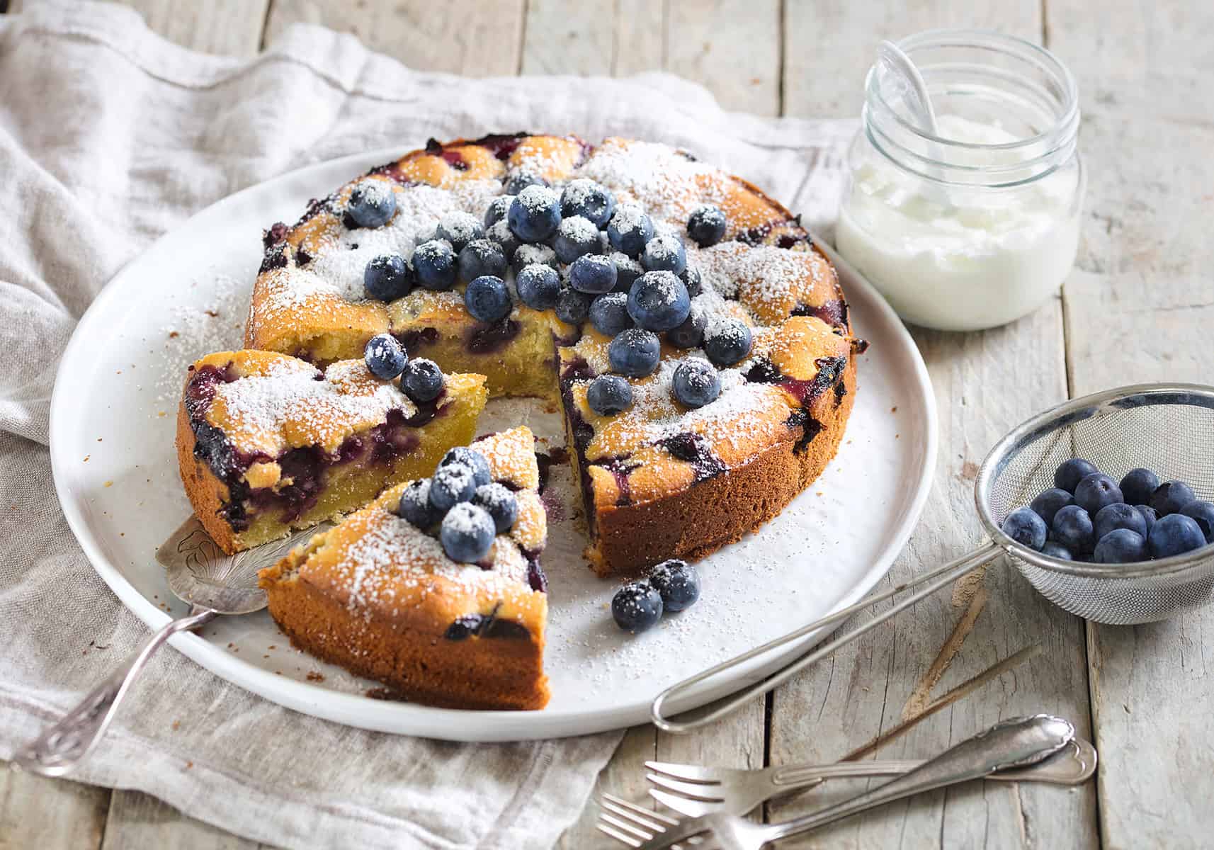 Blaubeerkuchen auf einem weißen Teller, angeschnitten