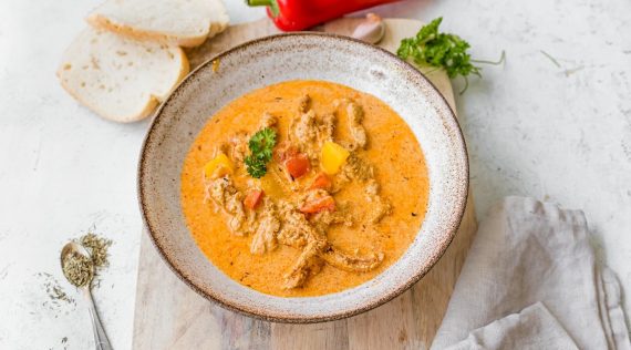 Ein Teller mit orangefarbener Suppe, die helles Fleisch enthält, von oben fotografiert – Foto: Sandra Leibinger