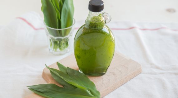 Eine Flasche Bärlauchöl auf einem Holzbrett, daneben frische Bärlauchblätter