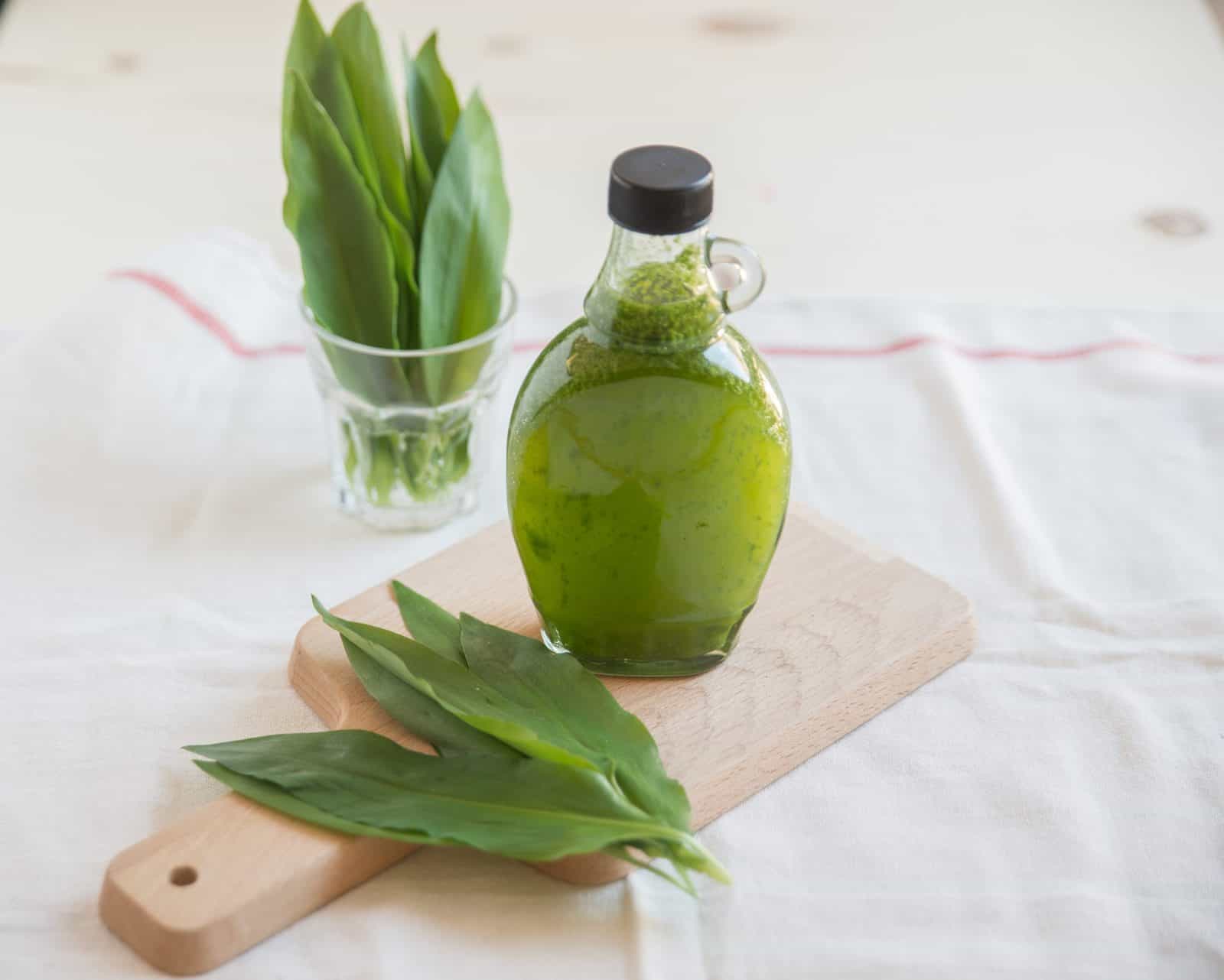 Eine Flasche Bärlauchöl auf einem Holzbrett, daneben frische Bärlauchblätter