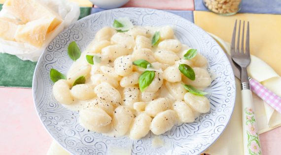 Gnocchi mit Käsesoße auf einem weißen Teller mit Basilikum garniert