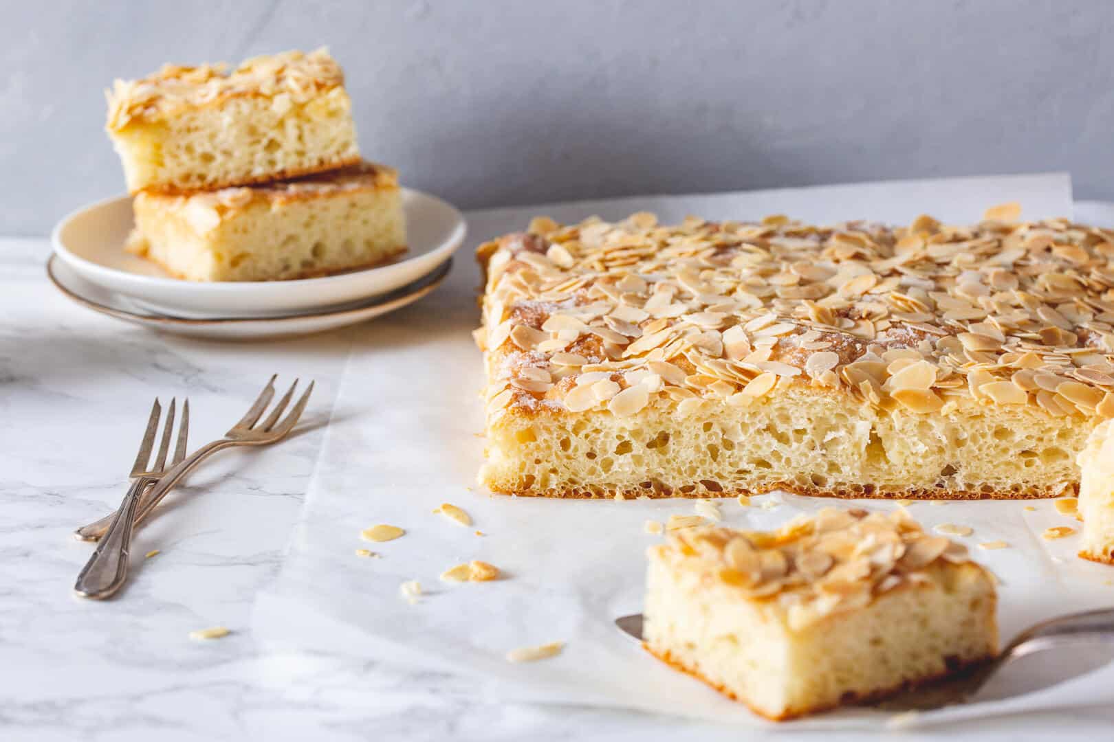 Butterkuchen vom Blech auf hellem Untergrund, mehrere Stücke abgeschnitten