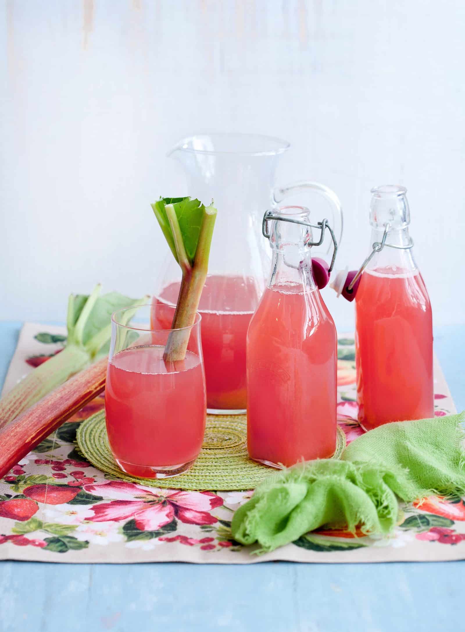 Drei Flaschen Rhabarbersaft und ein Glas mit einer Stange Rhabarber