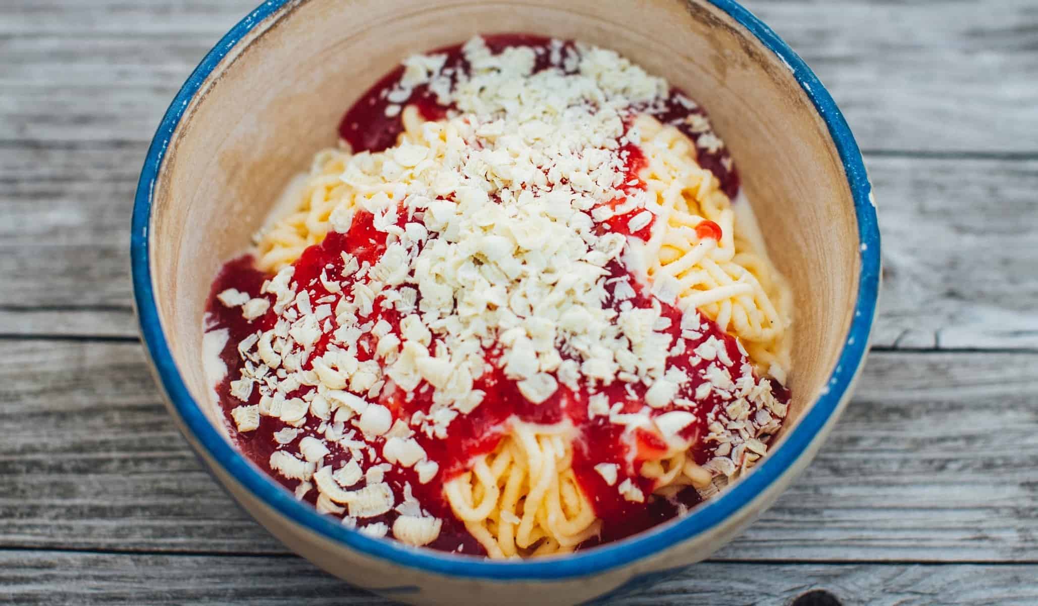 Spaghettieis mit Erdbeersoße und weißen Schokoraspeln in einer Schüssel von oben fotografiert