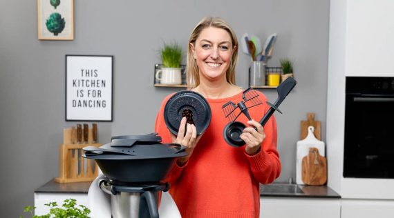 Dési von mein ZauberTopf steht neben dem Thermomix® und hält Zubehör hoch– Foto: Anna Gieseler