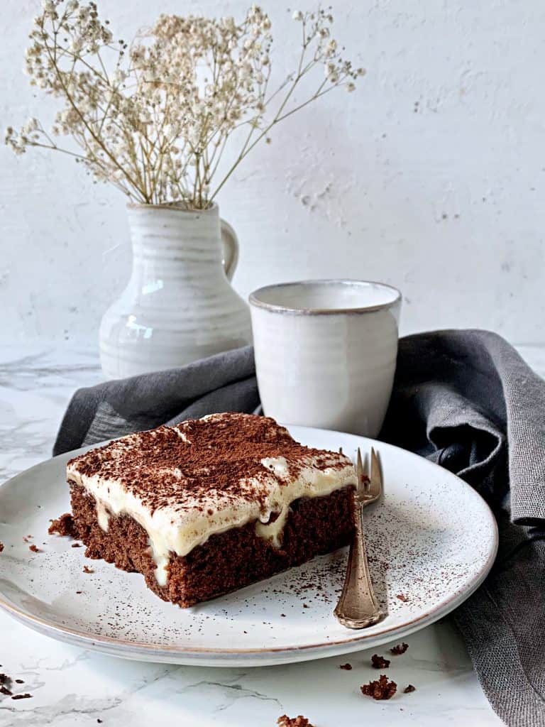 Ein Stück Schoko-Poke-Cake mit Creme-Topping auf einem weißen Teller – Foto: Karen Krüger