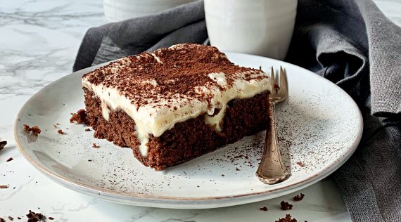 Ein Stück Schoko-Poke-Cake mit Creme-Topping auf einem weißen Teller – Foto: Karen Krüger