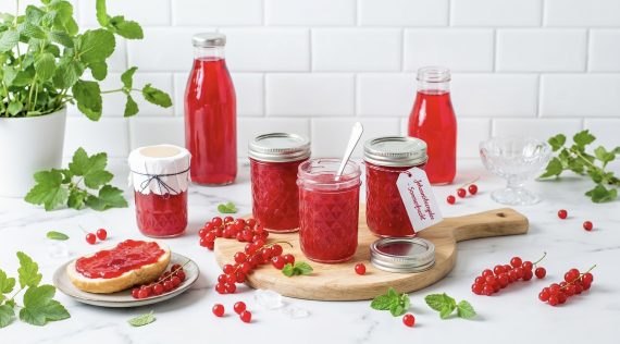 Mehrere Gläser mit rotem Gelee, umgeben von Johannisbeeren