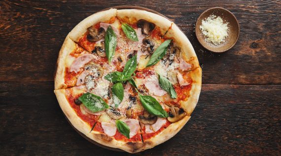 Pizza Prosciutto e funghi mit Parmesan und Basilikum garniert auf dunklem Untergrund