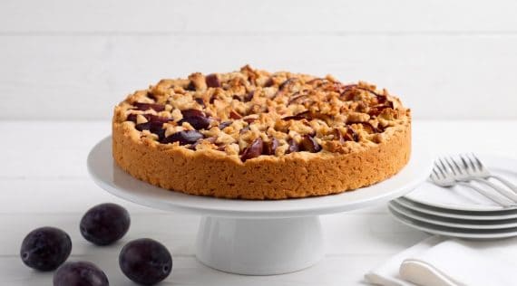 Pflaumenkuchen mit Streuseln auf einer weißen Tortenplatte