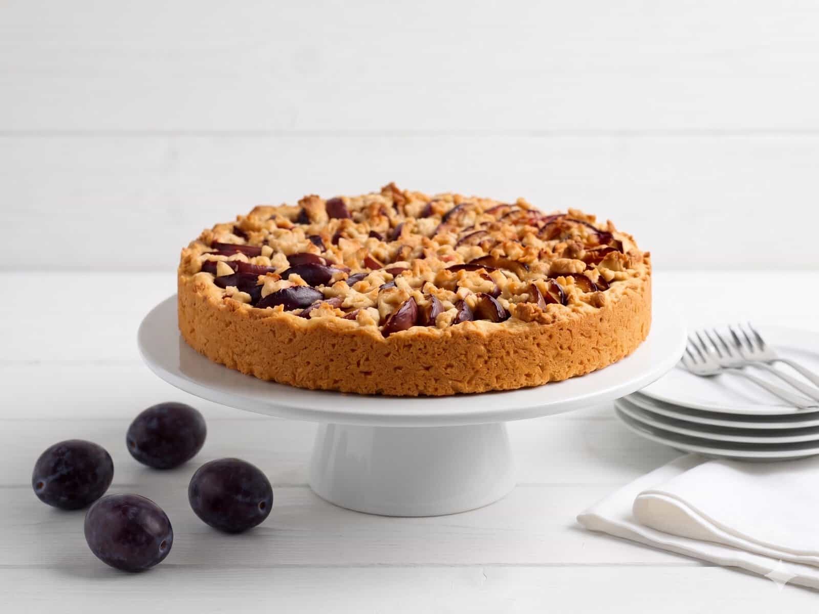 Pflaumenkuchen mit Streuseln auf einer weißen Tortenplatte