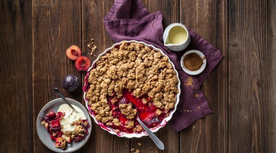 Apfel-Pflaumen-Crumble auf einem Holz-Untergrund von oben fotografiert