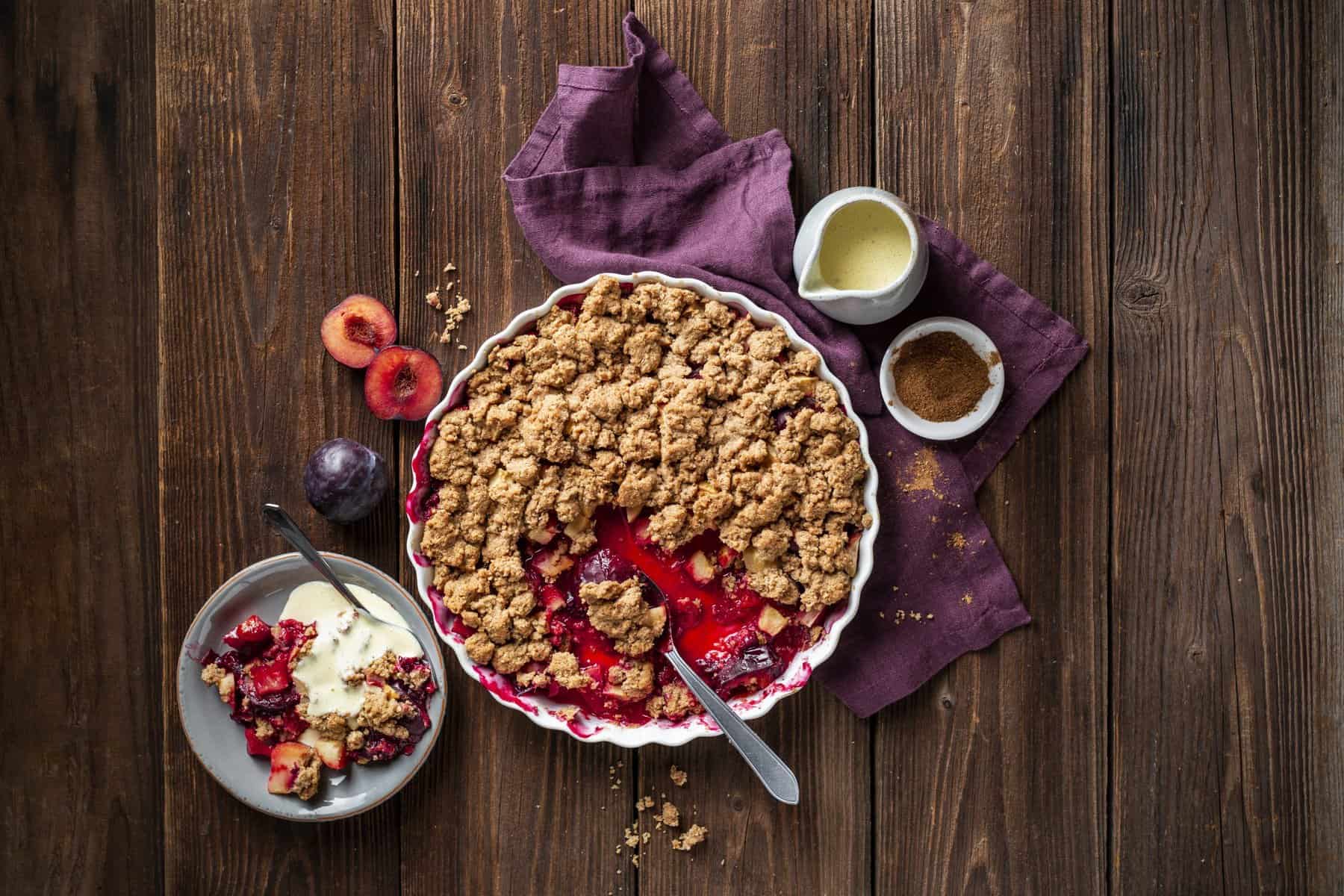 Apfel-Pflaumen-Crumble auf einem Holz-Untergrund von oben fotografiert