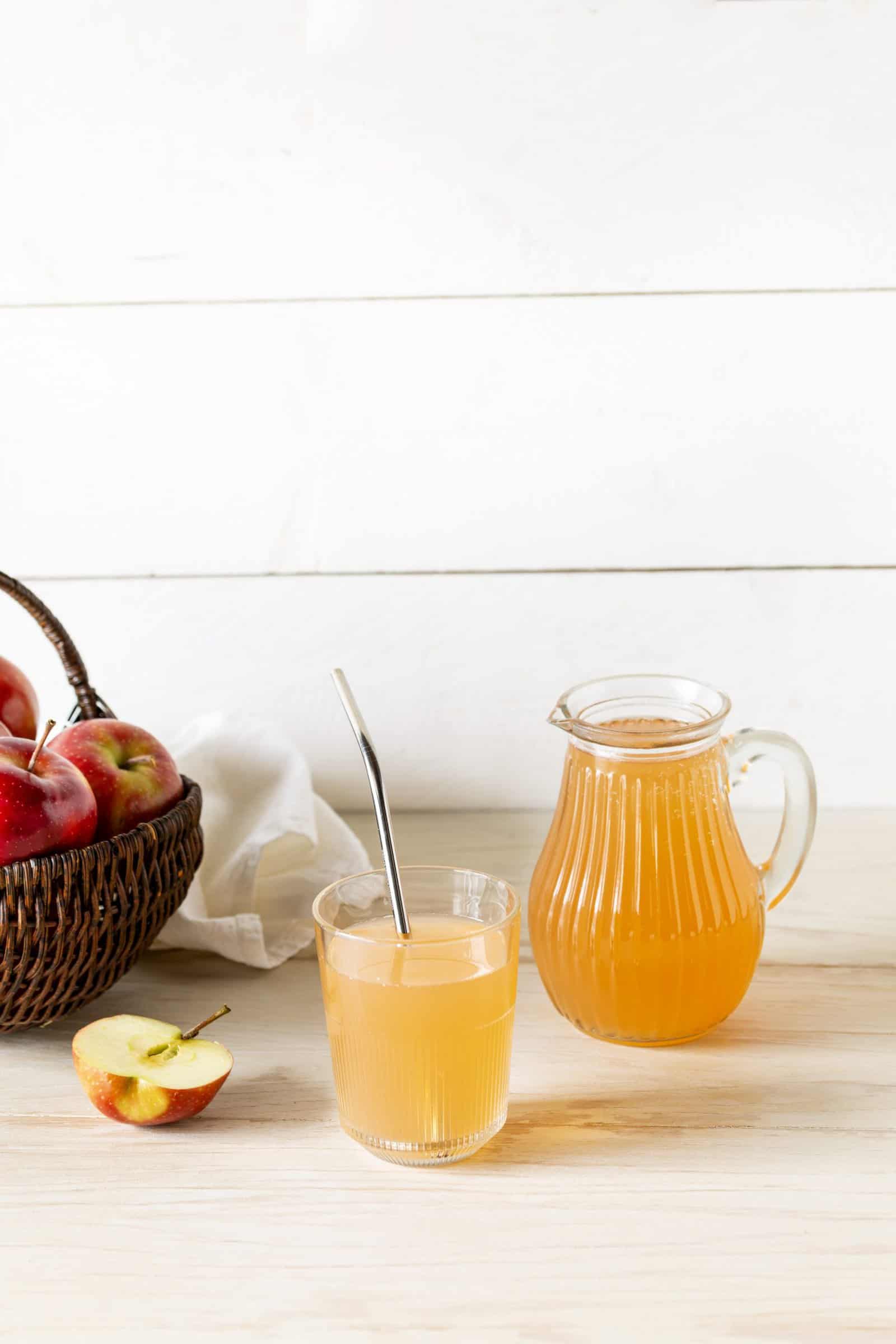 Apfelsaft in einer Karaffe, daneben ein Korb mit Äpfeln