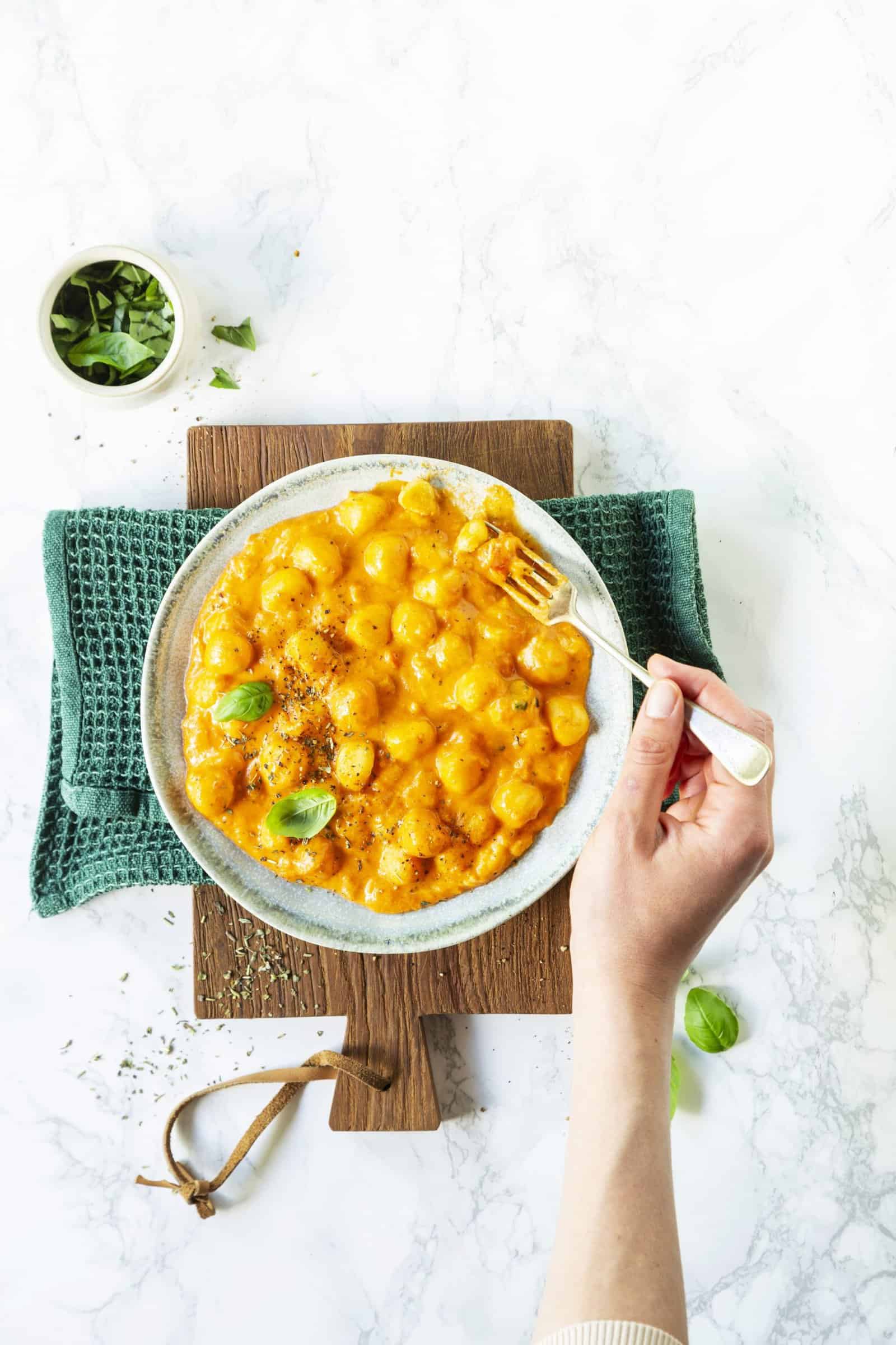 Tomate-Mozzarella-Gnocchi von oben fotografiert auf einem weißen Teller, der auf einem Holzbrett steht