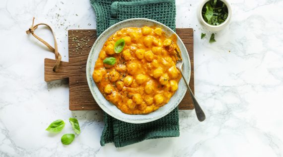 Tomate-Mozzarella-Gnocchi von oben fotografiert auf einem weißen Teller, der auf einem Holzbrett steht