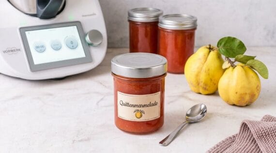 Drei Gläser mit orangefarbener Quittenmarmelade, daneben Quitten und ein Thermomix®