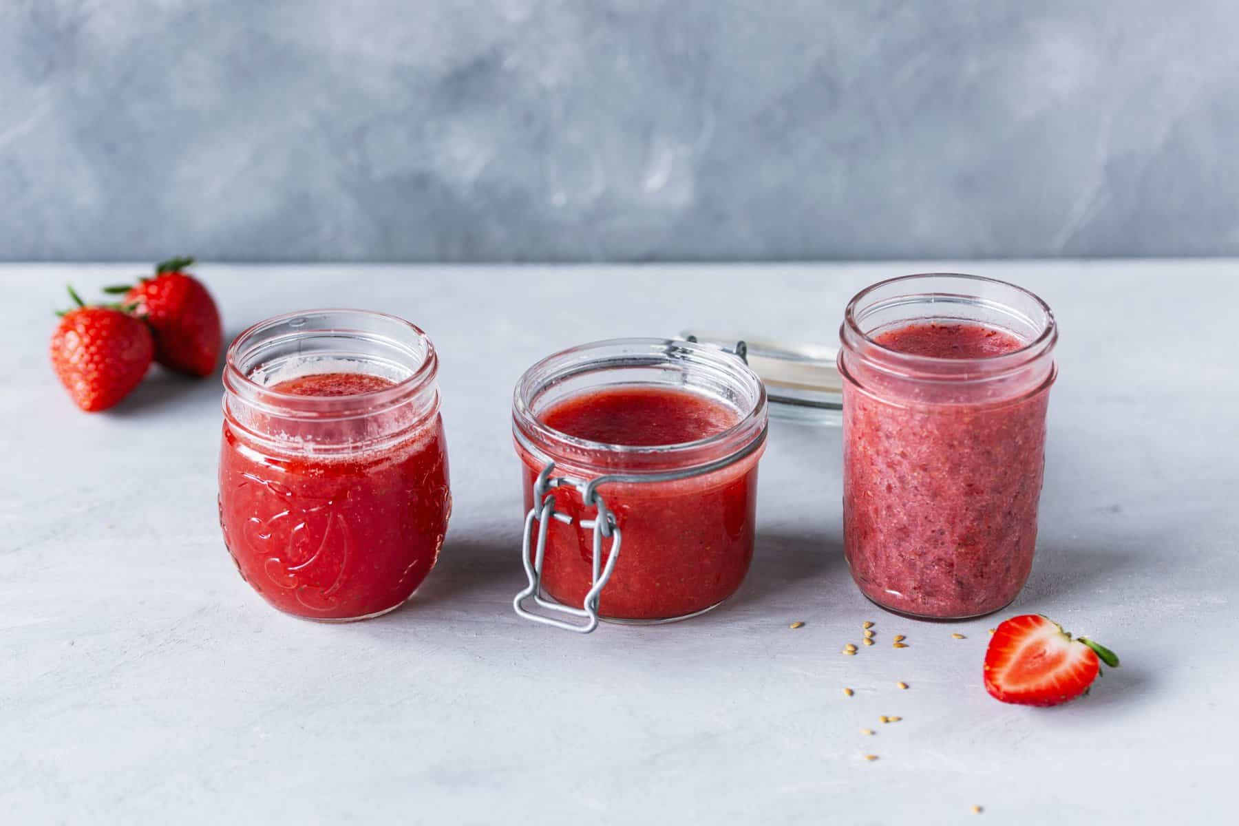 Drei Gläser mit Erdbeermarmelade, daneben Erdbeeren