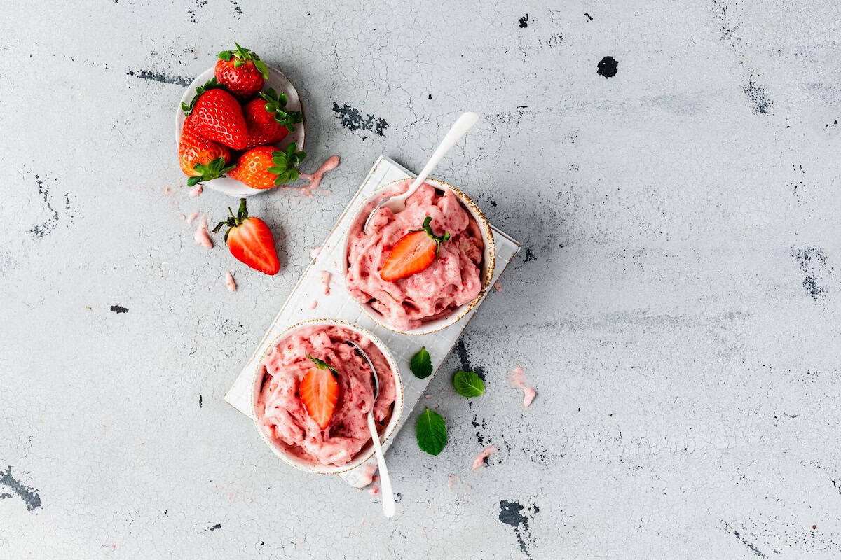 Zwei Schalen mit Erdbeereis von oben fotografiert, daneben frische Erdbeeren