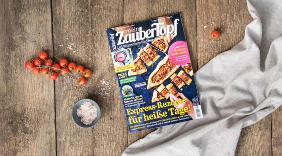 Die neue Ausgabe von mein ZauberTopf 5-2023 – das Magazin liegt auf einem Holztisch, daneben ein Tuch und Tomaten