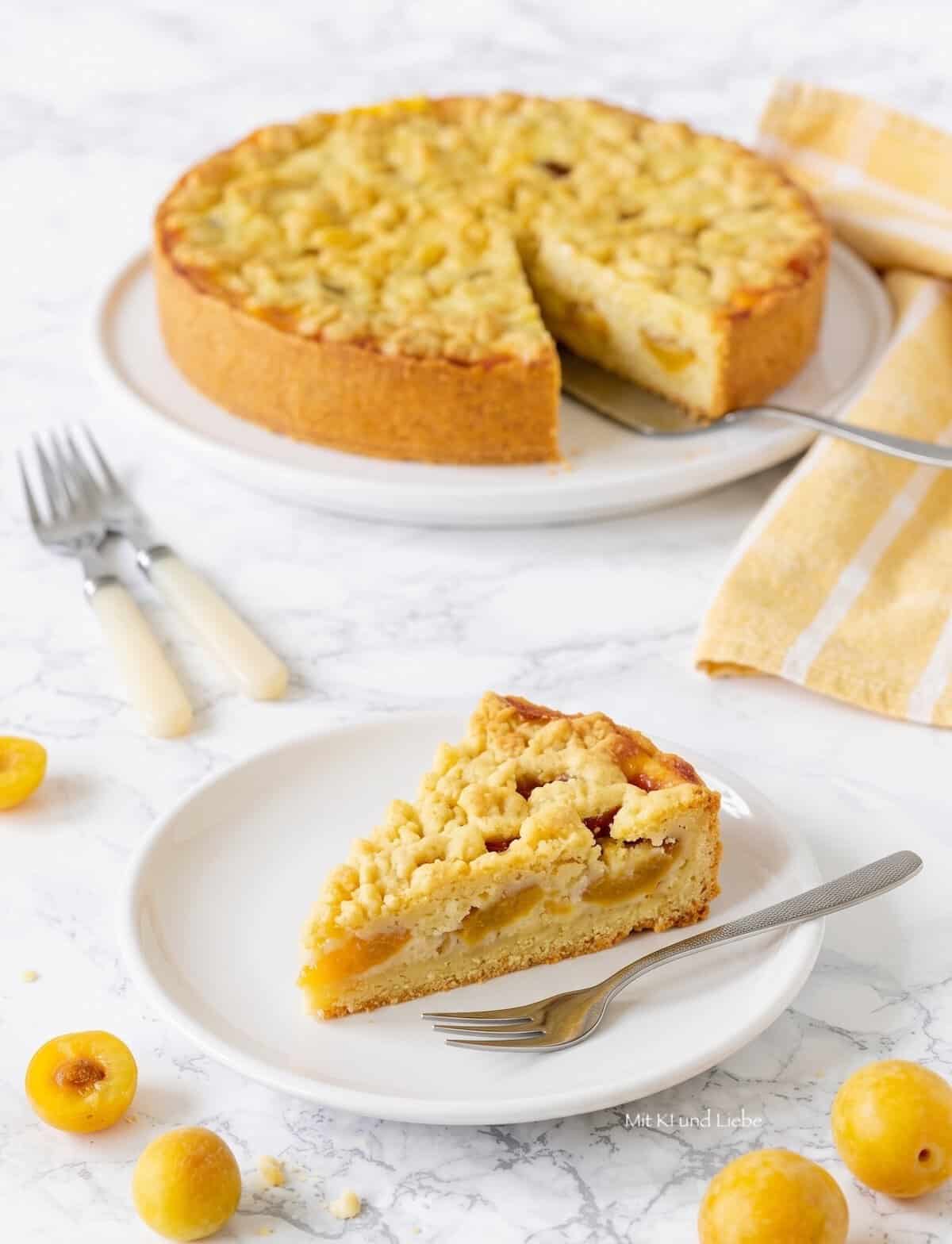 Ein Streuselkuchen mit Mirabellen darin auf einem weißen Teller, davor ein einzelnes Stück